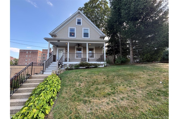 View of front facade featuring a porch, a front lawn, ceiling fan, and stairway