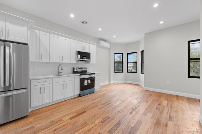 Kitchen featuring recessed lighting, appliances with stainless steel finishes, white cabinetry, light wood-style flooring, and a wall unit AC