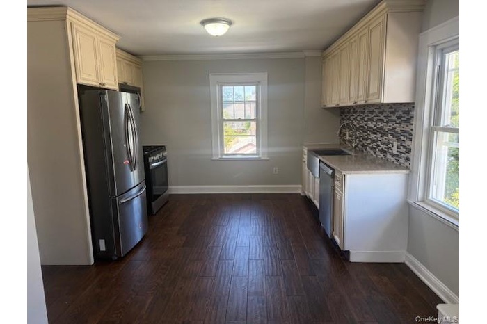 Kitchen featuring plenty of natural light, appliances with stainless steel finishes, backsplash, dark wood-type flooring, and crown molding