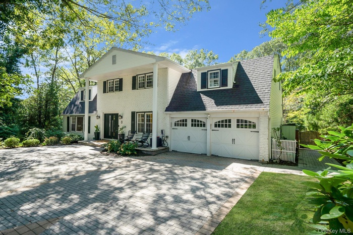 Greek revival house featuring decorative driveway, roof with shingles, a gate, and brick siding