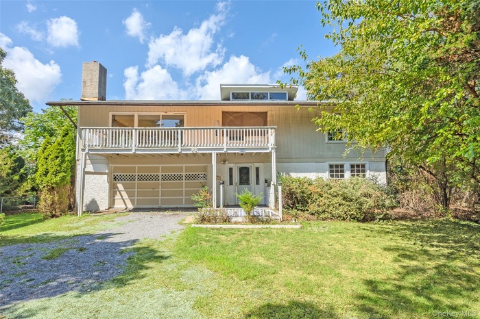 View of front of home featuring a front yard, driveway, a chimney, a balcony, and an attached garage