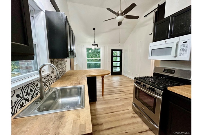 Kitchen with dark cabinetry, gas range, white microwave, light wood finished floors, and lofted ceiling