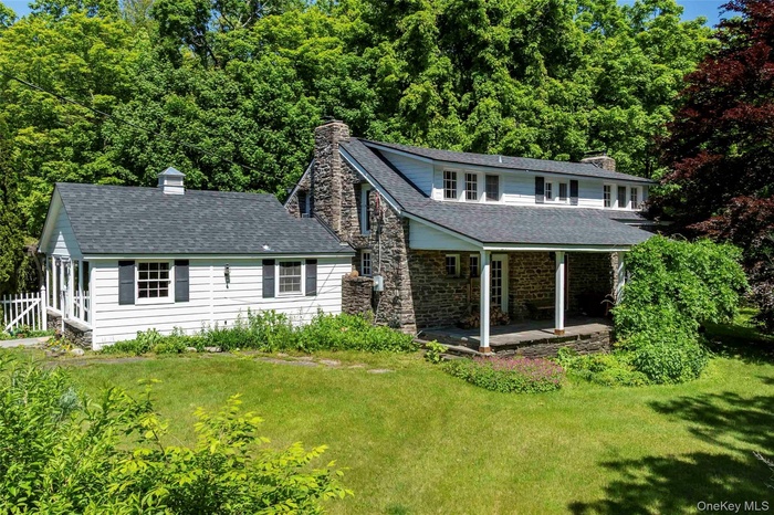 View of front of home featuring a chimney, a front lawn, stone siding, and a shingled roof