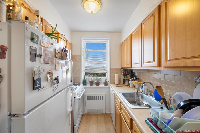 Kitchen featuring white appliances, light countertops, radiator heating unit, light wood-type flooring, and brown cabinetry