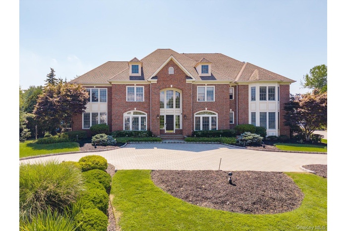 View of front of home featuring brick siding, curved driveway, and a front yard