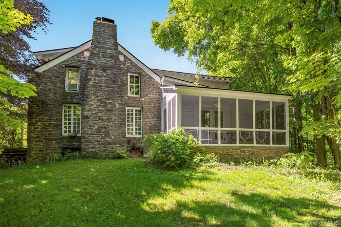 Back of property with stone siding, a chimney, a yard, and a sunroom
