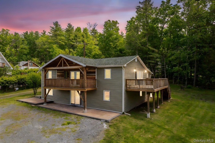 Front and side of house at dusk featuring a wooden deck, a forest view, and a lawn