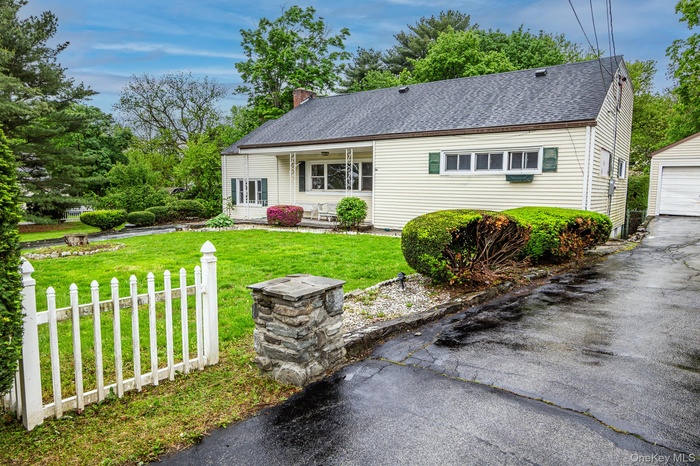 View of front facade featuring a front lawn, a detached garage, a chimney, roof with shingles, and an outbuilding