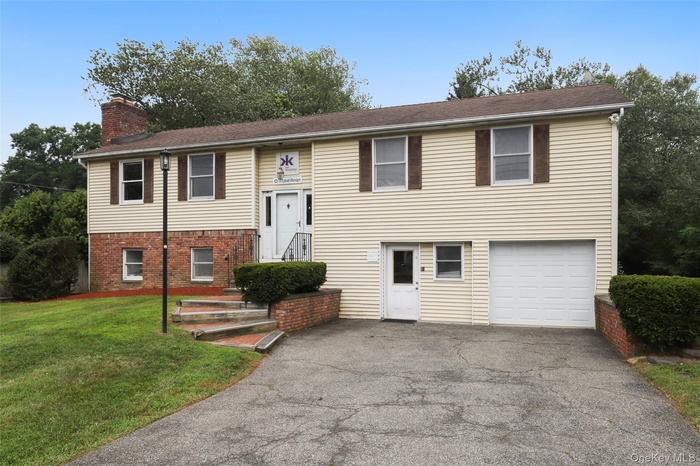 Bi-level home featuring driveway, brick siding, a chimney, an attached garage, and a front yard