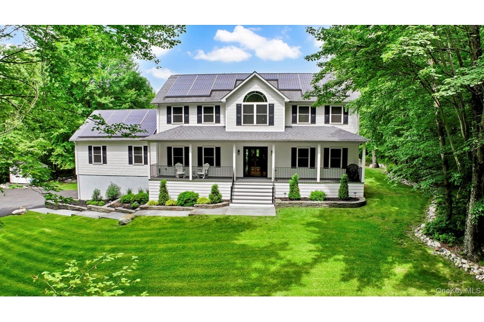 View of front of home with covered porch, solar panels, a front lawn, and roof with shingles