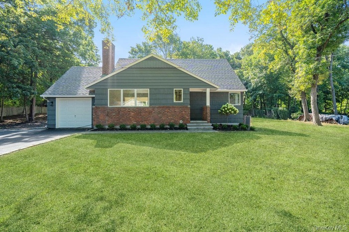 View of front of home featuring brick siding, a chimney, a front yard, newly paved driveway,