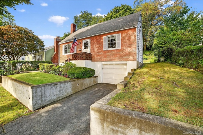 Bungalow-style house with a front lawn, brick siding, a chimney, driveway, and an attached garage