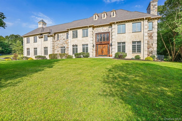 Georgian-style home featuring stone siding, a chimney, a front yard, and stucco siding