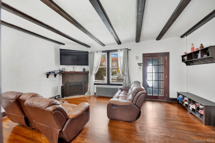 Living area with radiator heating unit, beamed ceiling, a brick fireplace, and wood finished floors