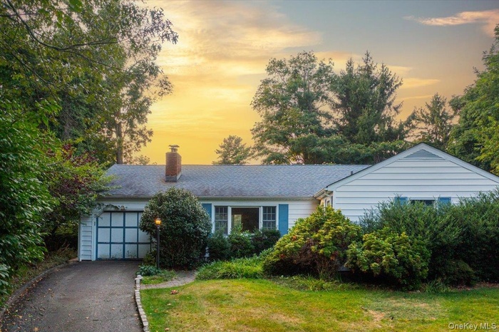 Ranch-style house featuring an attached garage, driveway, a chimney, and a yard