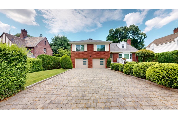 Tri-level home featuring brick siding, decorative driveway, a chimney, and an attached garage