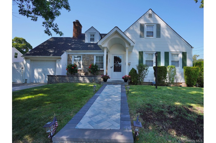 View of front facade featuring a front yard, a chimney, an attached garage, and roof with shingles