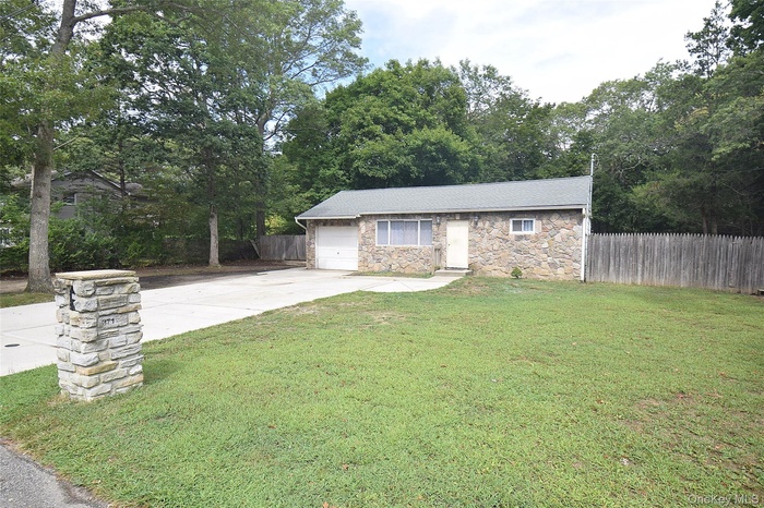 Ranch-style home with stone siding, view of wooded area, concrete driveway, and a garage