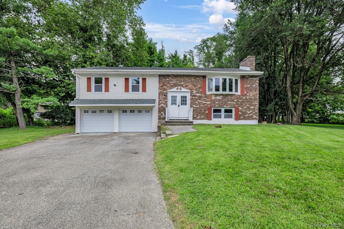 Raised ranch featuring asphalt driveway, a front lawn, a chimney, and brick siding