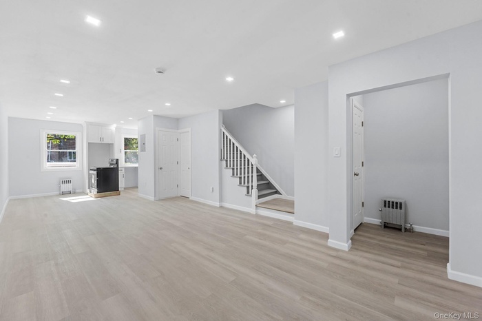 Unfurnished living room featuring recessed lighting, radiator heating unit, light wood finished floors, and stairway
