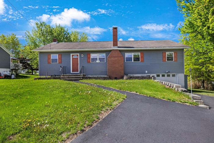 Single story home with entry steps, an attached garage, a chimney, and a front yard
