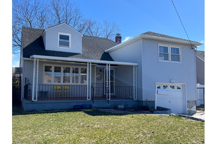 View of front of home with a front lawn, covered porch, a shingled roof, a garage, and a chimney
