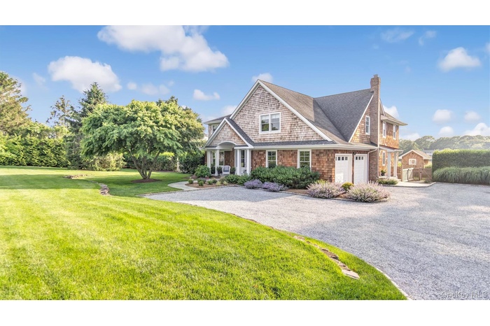 Shingle-style home with driveway, a chimney, a front lawn, and roof with shingles