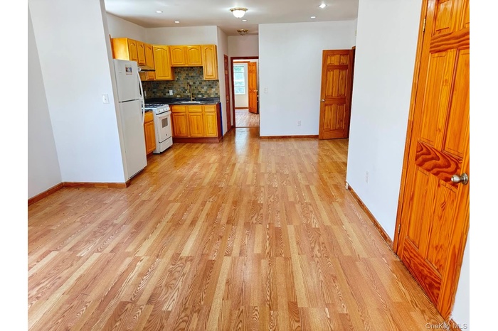 Kitchen with light wood-style floors, backsplash, white appliances, dark countertops, and recessed lighting