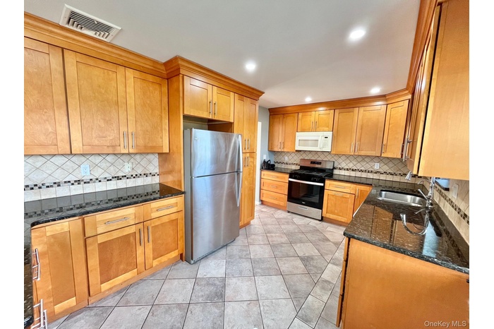 Kitchen with dark stone countertops, stainless steel appliances, tasteful backsplash, brown cabinetry, and recessed lighting