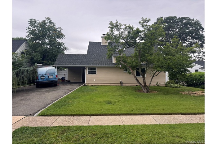 View of front of property featuring driveway, a front yard, roof with shingles, and a chimney
