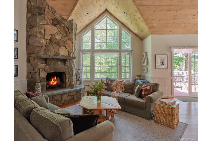 Living room with wainscoting, wood ceiling, a stone fireplace, high vaulted ceiling, and wood finished floors