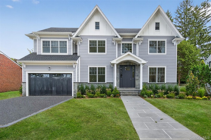 View of front of house with board and batten siding, an attached garage, a front lawn, driveway, and stone siding