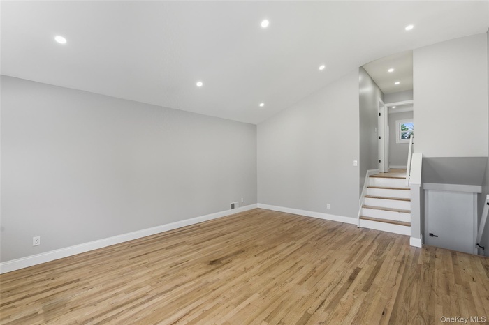 Unfurnished living room with recessed lighting, light wood finished floors, stairs, and lofted ceiling