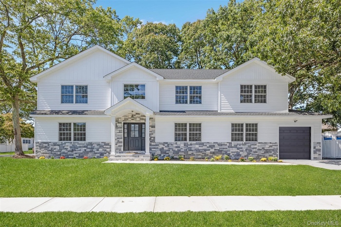 View of front of home featuring stone siding, a front yard, a shingled roof, and driveway