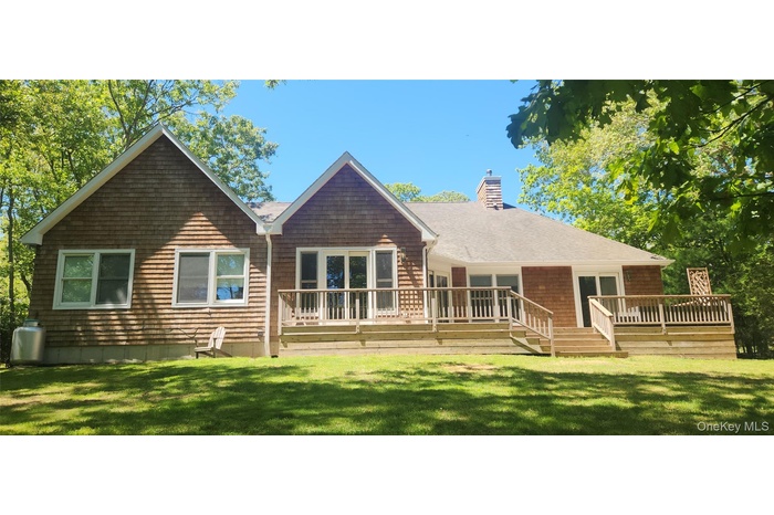Back of house featuring a chimney, a shingled roof, a lawn, and a wooden deck