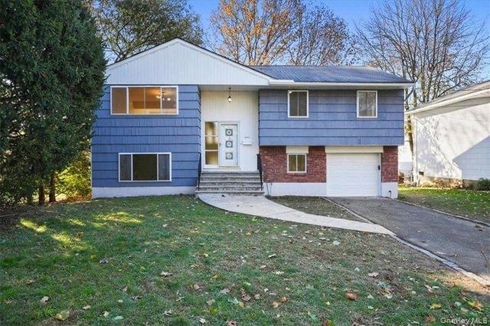 Split foyer home featuring brick siding, a garage, a front lawn, entry steps, and driveway
