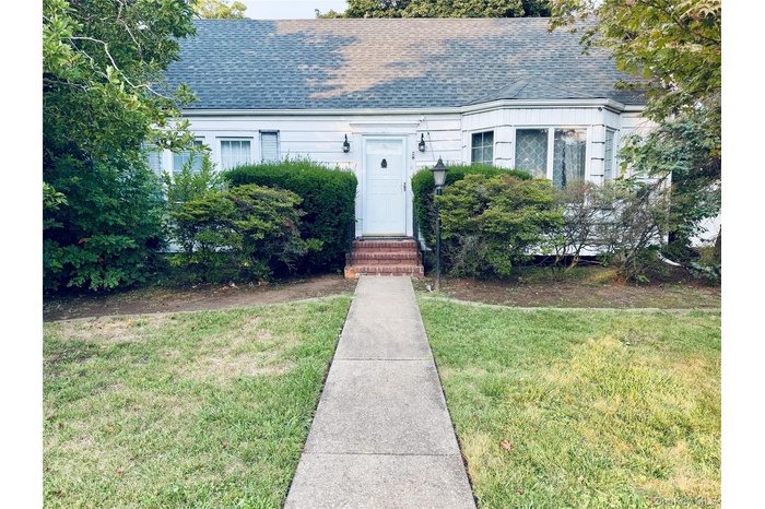 View of front facade with a front lawn, roof with shingles, and entry steps