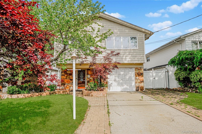 View of front of home with an attached garage, driveway, stone siding, and a gate