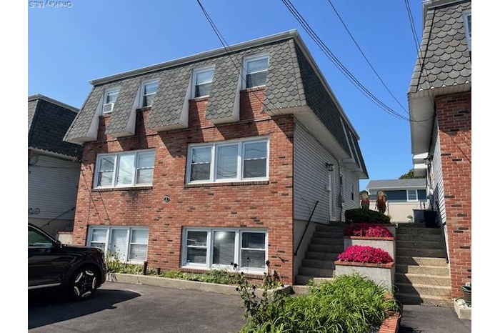 View of property exterior with brick siding, stairs, and mansard roof