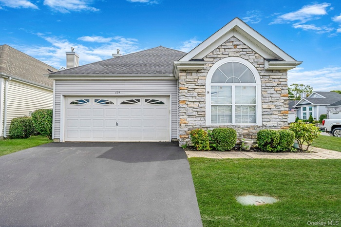 View of front facade with driveway, stone siding, a front yard, and a garage