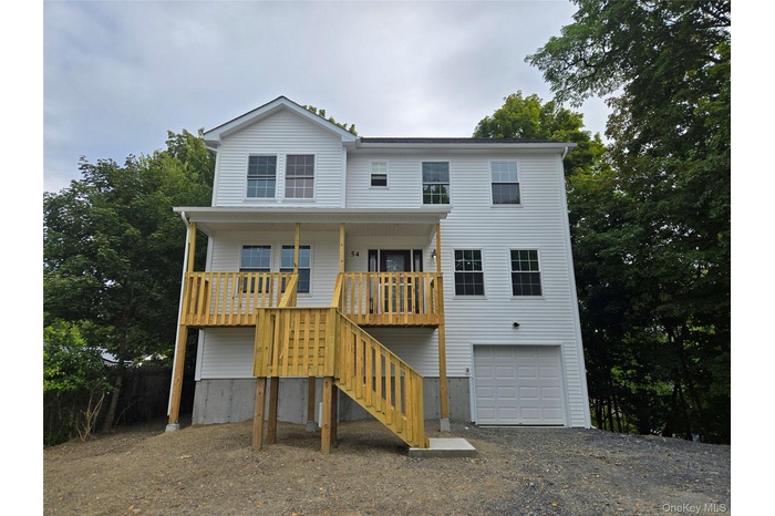 Coastal inspired home with stairway, an attached garage, gravel driveway, and a porch