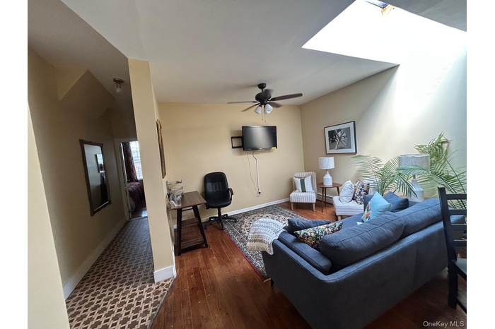 Living area with dark wood-style floors, ceiling fan, a skylight, and a baseboard heating unit