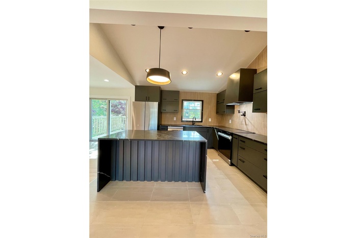 Kitchen featuring dark countertops, a kitchen island, fridge, wall chimney range hood, and pendant lighting