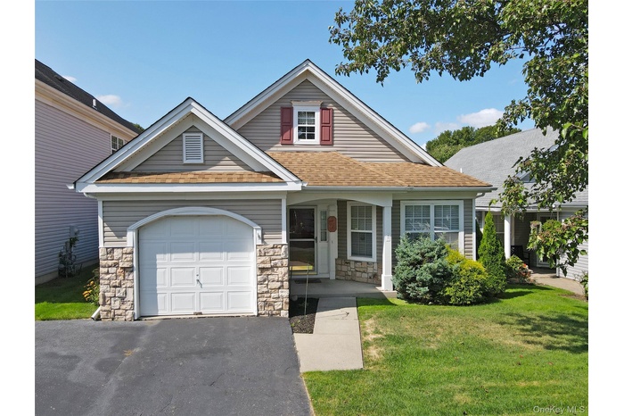 View of front of home with a front lawn, driveway, covered porch, a garage, and stone siding