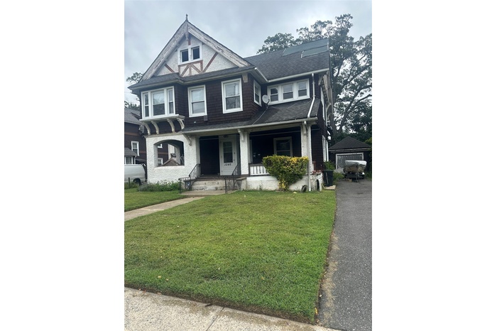 View of front facade with a porch, a front lawn, an outdoor structure, and roof with shingles