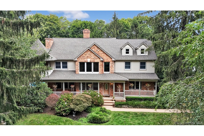 View of front facade with a porch, a shingled roof, brick siding, a chimney, and a front lawn