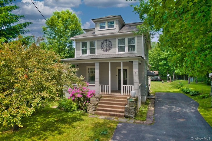 American foursquare style home with a porch, a front lawn, and roof with shingles