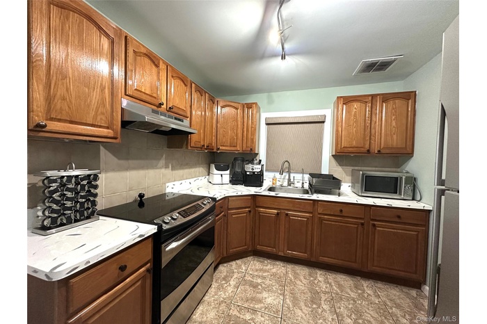 Kitchen with stainless steel appliances, backsplash, under cabinet range hood, and brown cabinets
