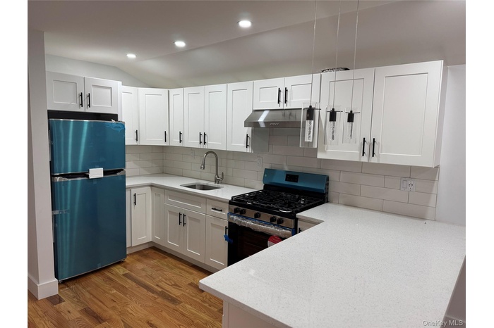 Kitchen featuring gas range, under cabinet range hood, a sink, light wood-style floors, and freestanding refrigerator