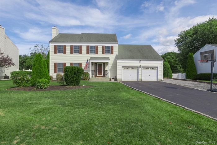 Colonial-style house featuring driveway, a garage, a shingled roof, a chimney, and a front yard